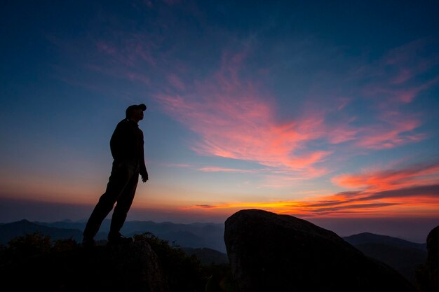 Silhouette man standing on rock against sky during sunset