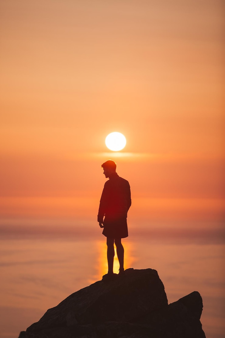 फोटो silhouette man standing on rock against sky during sunset