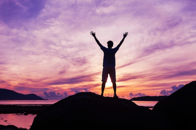 Silhouette man standing on rock against sky during sunset