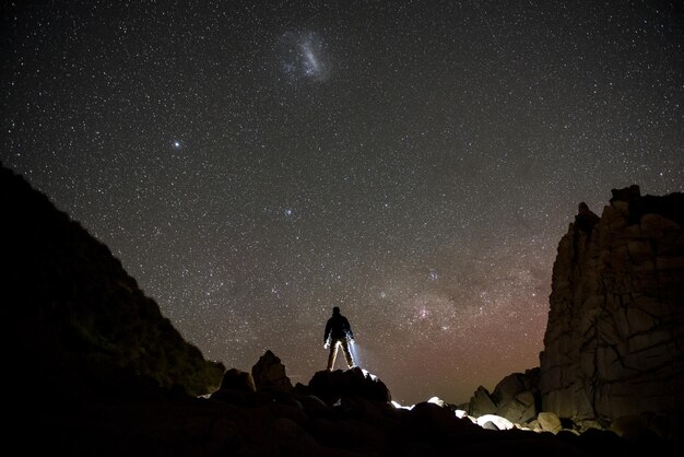 Foto silhouette uomo in piedi su una roccia contro il campo stellato di notte