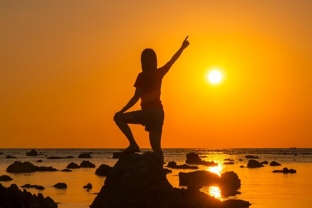 Photo silhouette man standing on rock by sea against sky during sunset