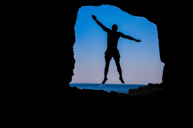 Foto silhouette uomo in piedi su una roccia dal mare contro il cielo