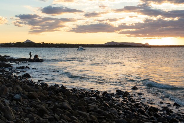 オーストラリアの海の夕日を見ている岩の上に立っている男のシルエット。旅行者の概念