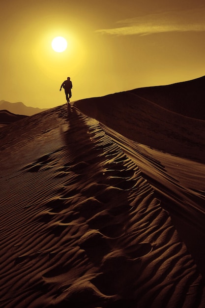 Photo silhouette man standing on sand at sunset