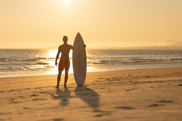 Silhouette of a man standing on the shore holding a surfboard