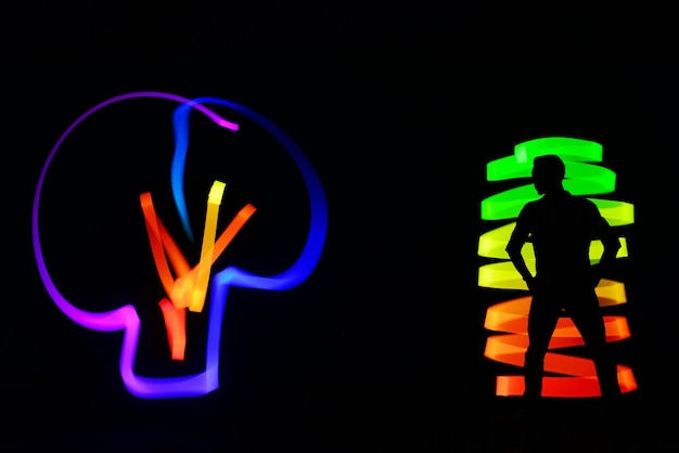 Photo silhouette man standing with colorful lighting paintings against black background
