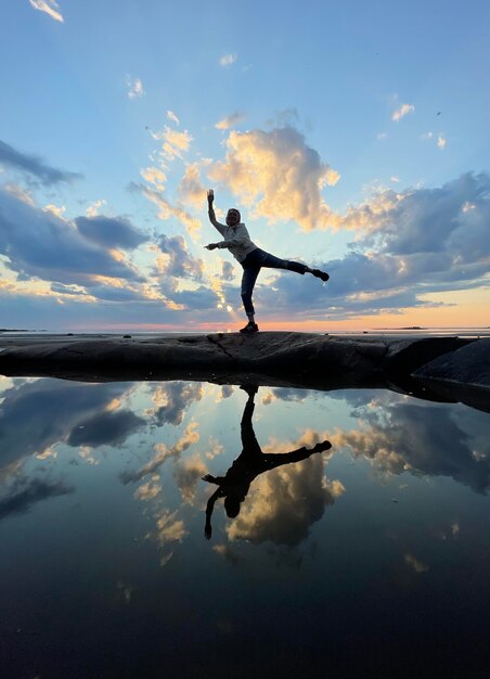 Photo silhouette of a man standing in a yoga pose in a lake against the sky during sunset