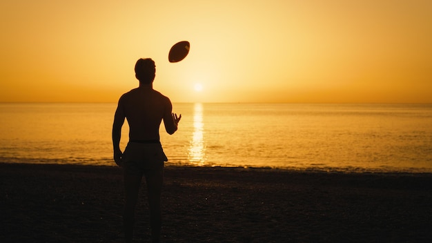 アメリカンフットボールのボールを持った夕暮れの男のシルエット