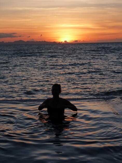 Foto silhouette uomo che nuota in mare contro il cielo durante il tramonto