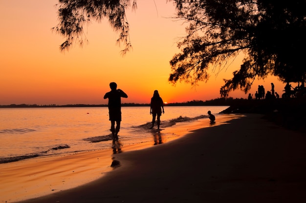 Siluetta dell'uomo che prende a maschera la sua amica sulla spiaggia al tramonto