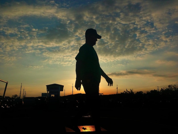 Foto silhouette uomo che cammina contro il cielo nuvoloso durante il tramonto