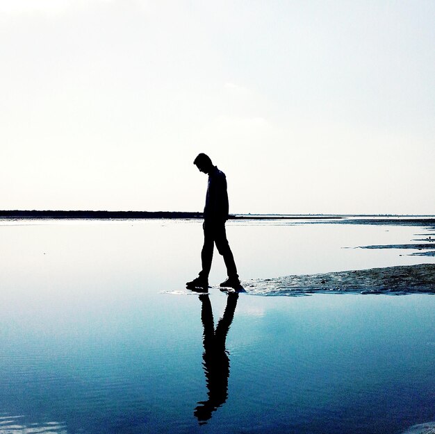 写真 明るい空に反射して岸を歩くシルエットの男