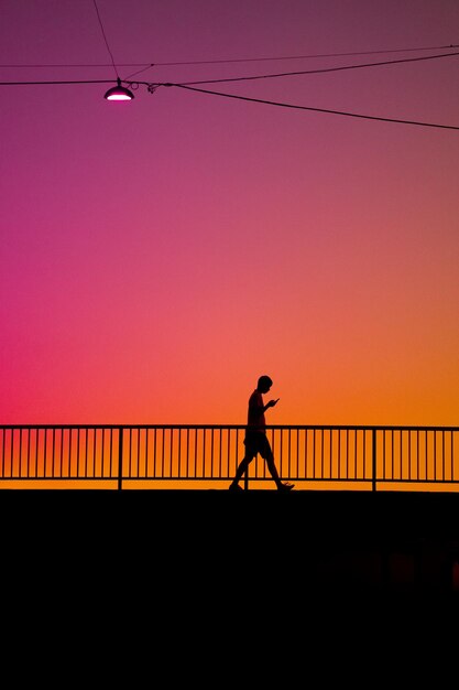 Silhouette man walking on pier against sky during sunset