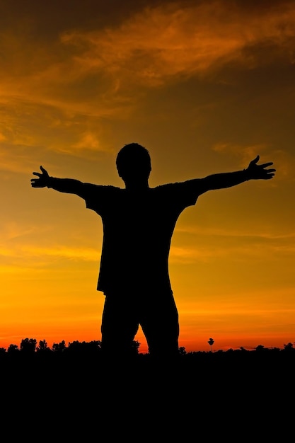 Photo silhouette man with arms outstretched standing against sky during sunset