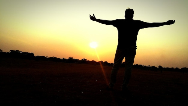 Фото Силуэт мужчины с вытянутыми руками, стоящего на поле при заходе солнца