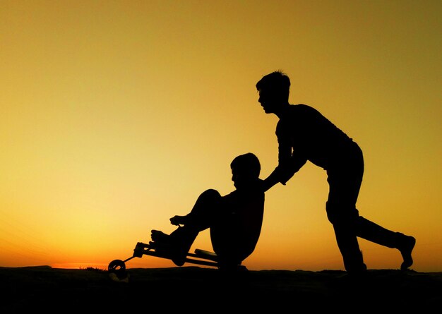 Photo silhouette man with arms raised against orange sky