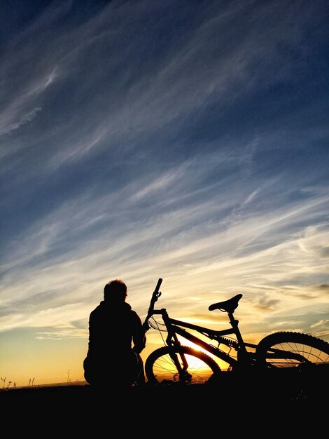 Silhouette man with bicycle against sky during sunset