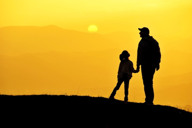 Silhouette man with daughter standing on land against orange sky