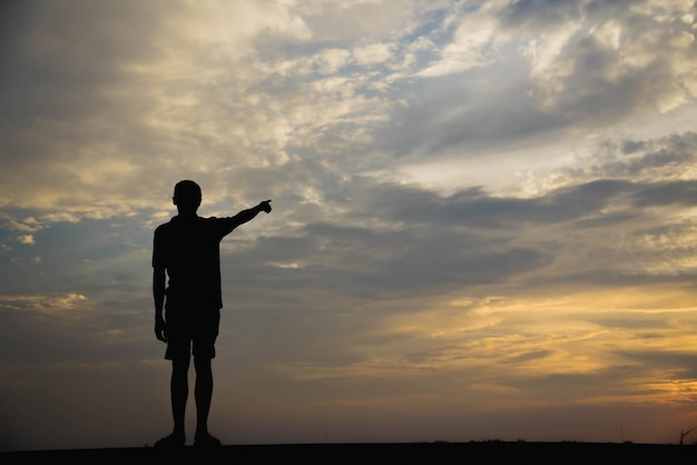 Silhouette of a man with hands point to sky in the sunset.