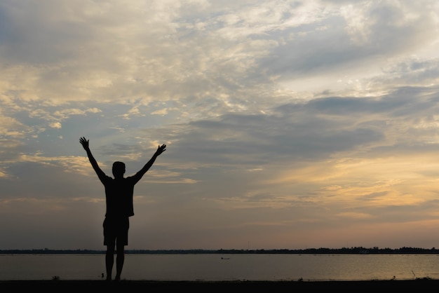 Siluetta di un uomo con le mani alzate al tramonto.