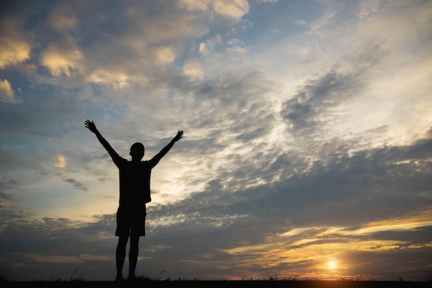 Silhouette of a man with hands raised in the sunset.