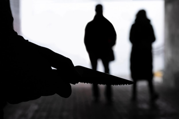 Foto silhouette di un uomo con un coltello sullo sfondo di persone in un tunnel oscuro concetto di crimine di violenza