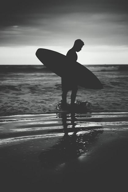 Foto uomo a silhouette con tavola da surf in piedi sulla spiaggia contro il cielo durante il tramonto