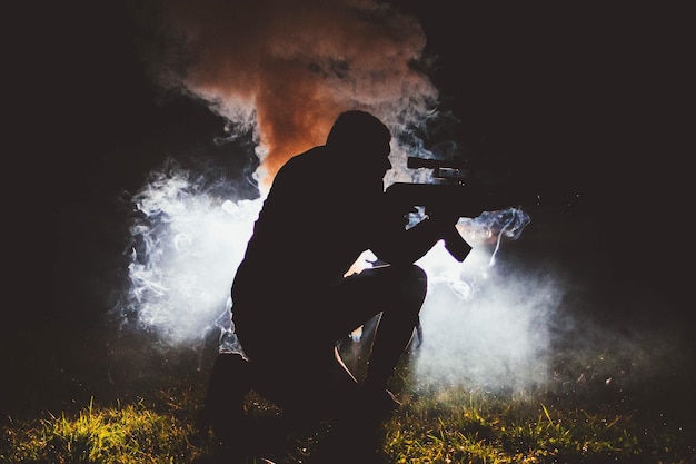 写真 銃を持ったシルエットの男が夜にフィールドでひざまずいている