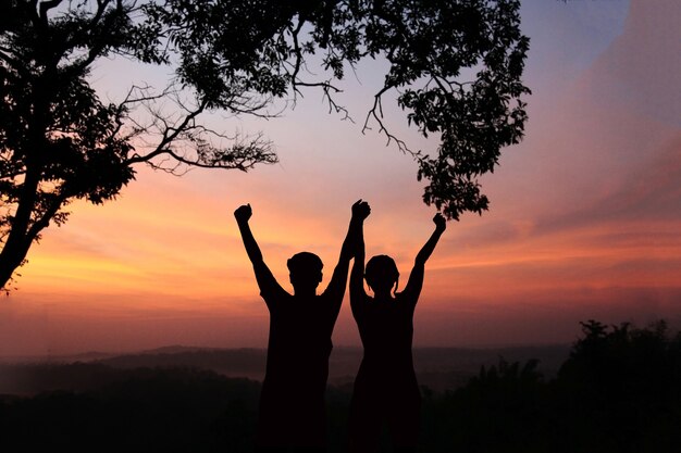 silhouette of man and women show arm up for achievements successful and celebrating success with sun