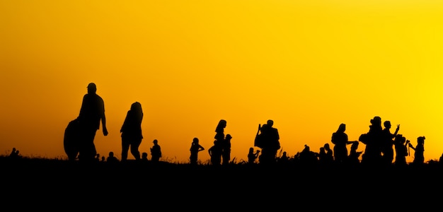 Силуэт многих туристов фотографируют на смартфон на вершине горы во время заката.
