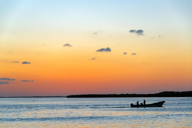 夕暮れの空に照らされた海上のボートのシルエットの男性