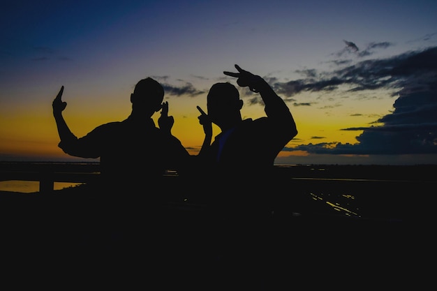 Foto uomini a silhouette che fanno gesti contro il cielo durante il tramonto