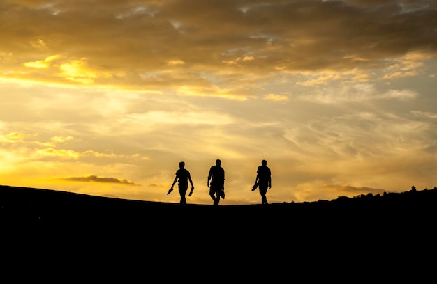 Silhouette men walking on hill against sky during sunset