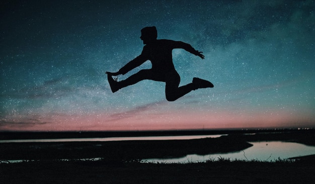 Silhouette mid adult man jumping on field against star field at night