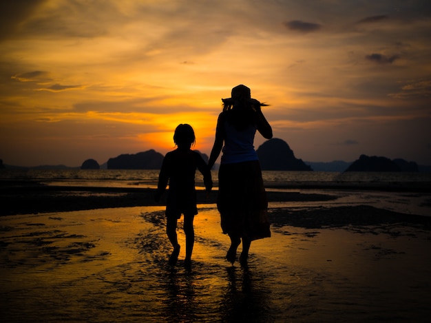 Силуэт матери, проведение доброй руки и прогулки по пляжу во время заката