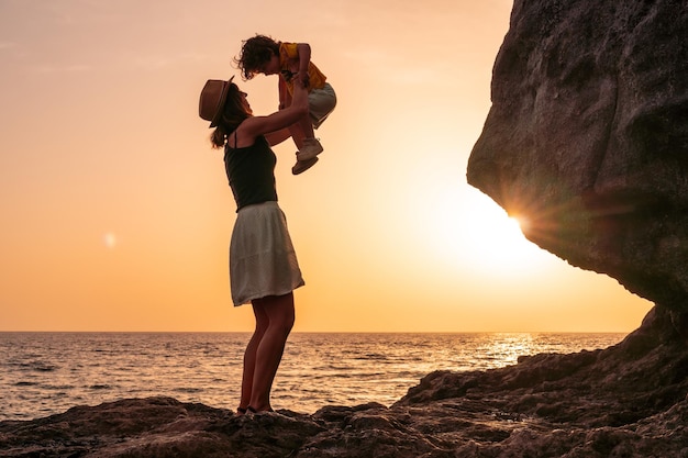 エル・イエロ島カナリア諸島のタコロンのビーチで息子を夕日に持ち上げて楽しんでいる母と息子のシルエット休暇のコンセプトオレンジ色の夕日