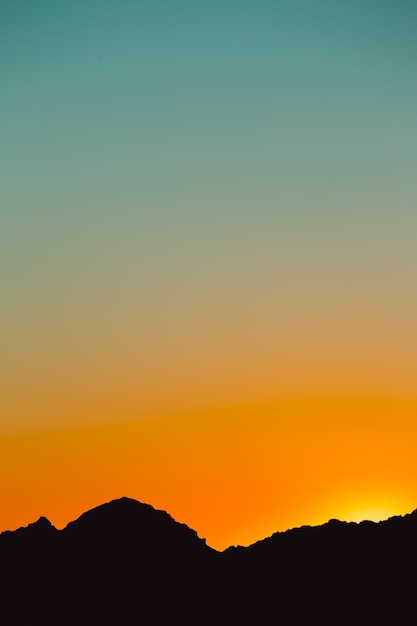 A silhouette of a mountain in black with a sunset sky gradient in orange and blue