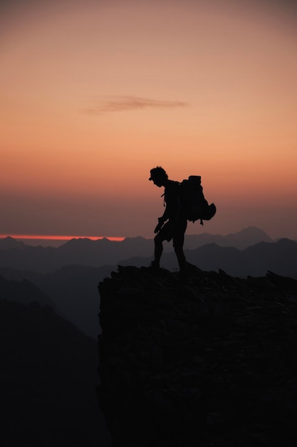 Foto silhouette di un alpinista in un'alba calda e colorata su una roccia nei pirenei che guarda il paesaggio mentre fa arrampicata e alpinismo nei pirenei