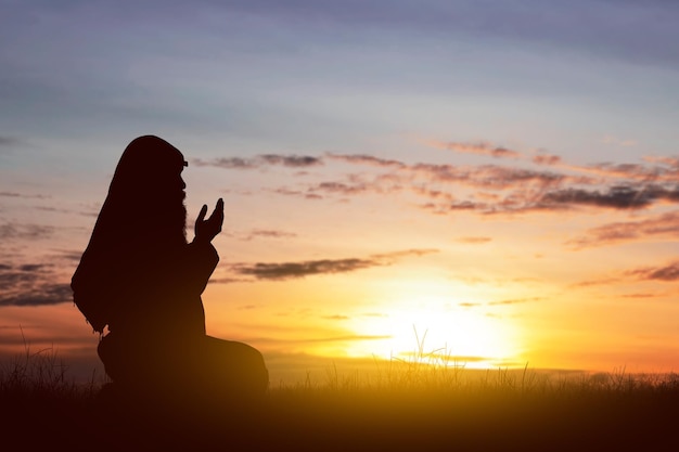 Silhouette of a Muslim man with a beard wearing keffiyeh with agal in praying while raised hands