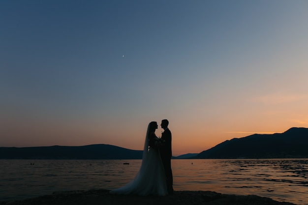 Silhouette of a newlywed couple at the sea at sunset wedding in