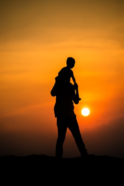Фото Силуэт семьи с мальчиком, счастливо катающимся на шее своего отца на фоне закатного неба