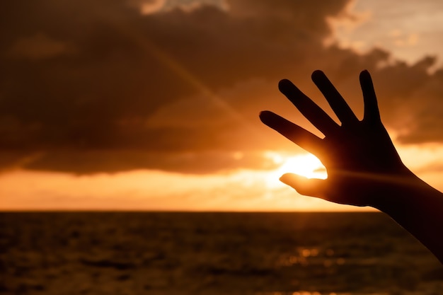 Фото Силуэт руки, поднятой к небу море и вечернее солнце, сумерки