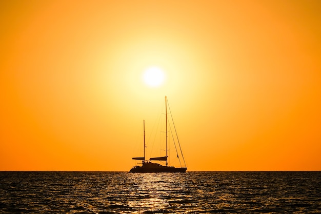 写真 夕日の地平線の背景に海で2本マストのヨットのシルエット。