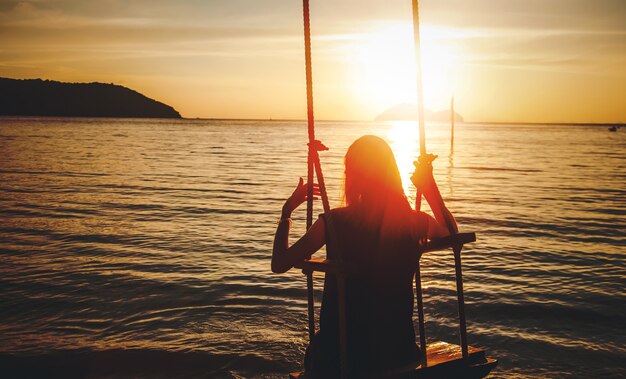 写真 夕暮れ時の海、休暇を見て瞑想自然とソロ旅行の概念のブランコに乗る女性のシルエット