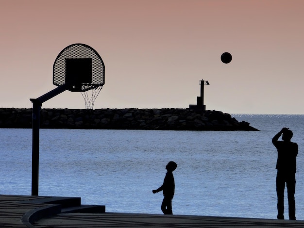 写真 夕暮れの空に照らされた海のバスケットボール選手のシルエット