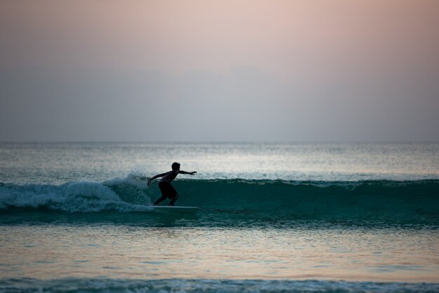 日没時に海の海岸でサーフィンをしている少年のシルエット