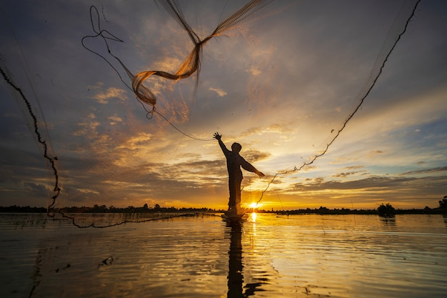 写真 夕暮れ時の湖のネットで漁船の漁師のシルエット