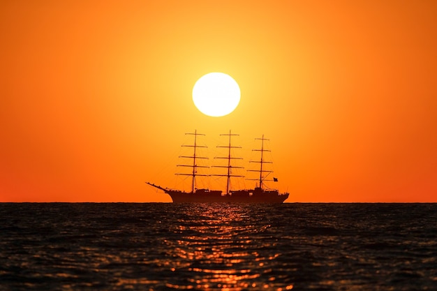 Фото Силуэт трехмачтового корабля херсонес в море на фоне оранжевого закатного неба и солнца.
