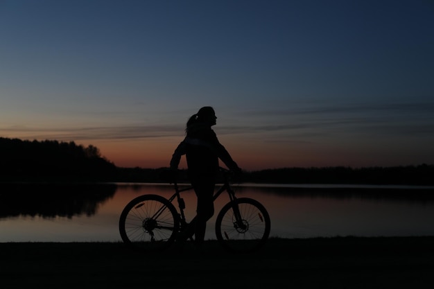 写真 カラフルな青い空の夕日の背景にマウンテンバイクと女性のシルエットアクティブな屋外のライフスタイル