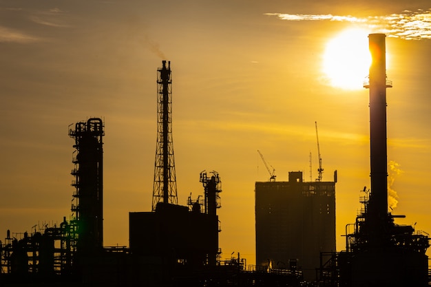 Foto siluetta della pianta di industria della raffineria di petrolio e gas con illuminazione di scintillio e alba di mattina
